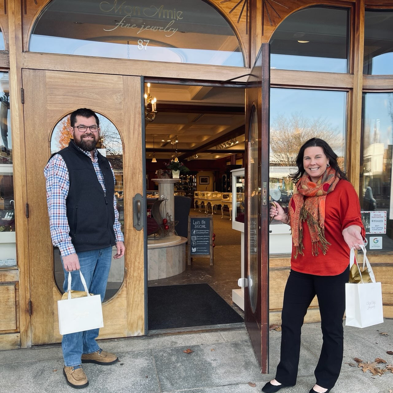 Pictured: Amie and Ron, owners of Mon Amie Fine Jewelry holding the door open in the front of the store.